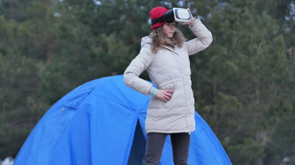 Atractiva joven turista con sombrero rojo se sienta en una carpa turística y disfruta de un casco de realidad virtual — Foto de Stock