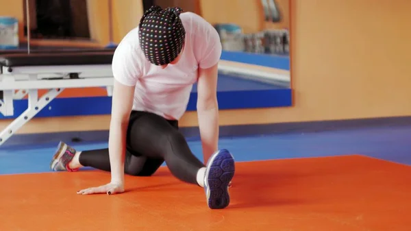 Een aantrekkelijke vrouw doet zich uitstrekt op een simulator in een sportschool sport — Stockfoto