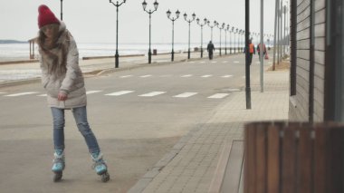 Sportif sıcak giysiler ve Silindirler, deniz kenarı yolda sürme giyen genç güzel kadın kırmızı şapkalı