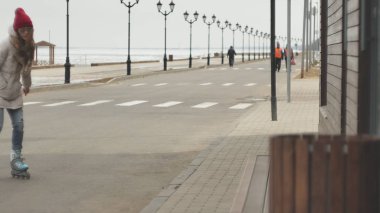 Sportif sıcak giysiler ve Silindirler, deniz kenarı yolda sürme giyen genç güzel kadın kırmızı şapkalı