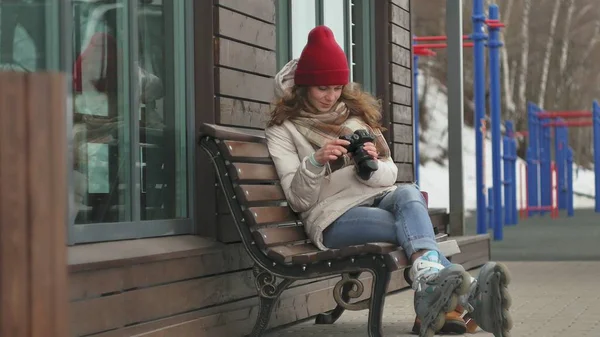 Junge schöne Frau mit rotem Hut in sportlich warmer Kleidung und Rollatoren, auf einer Holzbank sitzend und mit einer Vintage-Kamera fotografierend — Stockfoto