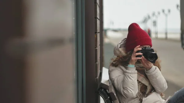 スポーティな暖かい服やビンテージ カメラで写真を撮ると木製のベンチに座って、ローラーを身に着けている赤い帽子の若い美しい女性 — ストック写真