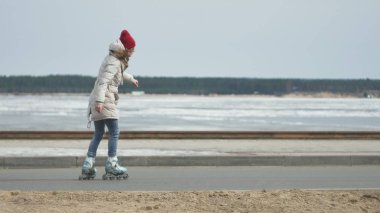 Sportif sıcak giysiler ve Silindirler, deniz kenarı yolda sürme giyen genç güzel kadın kırmızı şapkalı