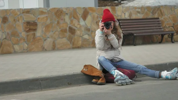 Kırmızı şapka giyen sportif sıcak giysiler ve silindirleri, asfalt yolda ve vintage fotoğraf makinelerinde fotoğraf çekimi oturan genç güzel kadın — Stok fotoğraf