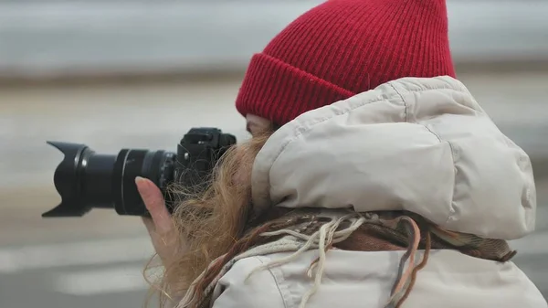 Young beautiful woman in red hat wearing sporty warm clothes and rollers, sitting on the asphalt road and taking pictures on a vintage camera — Stock Photo, Image