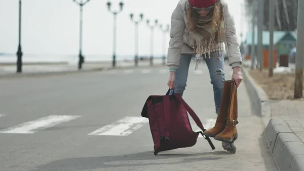 Fiatal gyönyörű nő egy piros sapkát visel, sportos meleg ruhát és a görgők, lovaglás a tengerparton úton — Stock Fotó