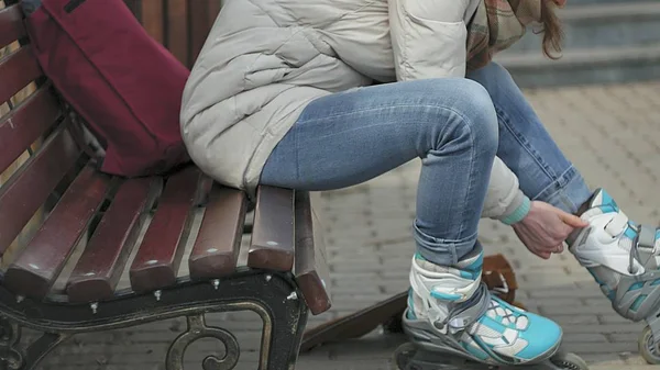 Giovane bella donna in abiti sportivi caldi e rulli, seduta su una panchina di legno e vestiti pattini a rotelle preparandosi con pattinaggio — Foto Stock