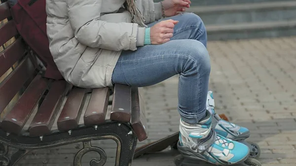 Joven mujer hermosa en ropa de abrigo deportivo y rodillos, sentado en un banco de madera y vestidos patines preparándose con patinaje — Foto de Stock