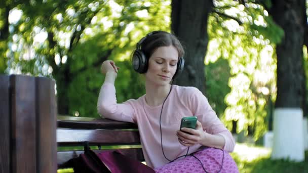 Joven mujer hermosa con estilo, en las calles de la ciudad escuchando música en los auriculares del monitor grande . — Vídeo de stock