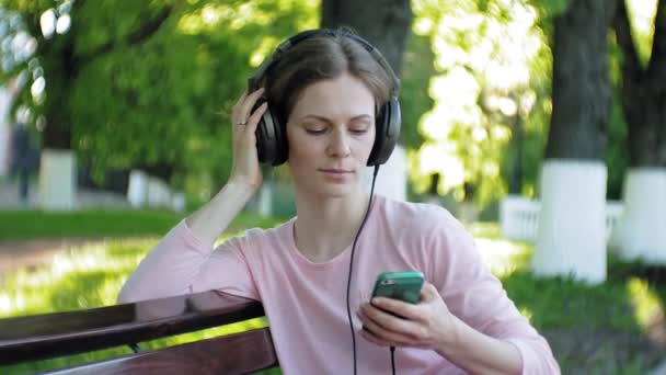 街の大型モニターのヘッドフォンで音楽を聴く上で若いスタイリッシュな美しい女性、. — ストック動画