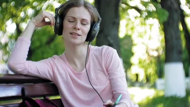 Stijlvolle mooie jongedame, op de straten van de stad luisteren naar muziek in de grote monitor hoofdtelefoon. — Stockvideo