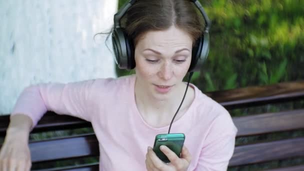 Jovem elegante mulher bonita, nas ruas da cidade ouvindo música em grandes fones de ouvido monitor . — Vídeo de Stock
