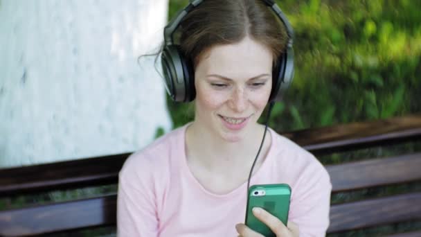 Joven mujer hermosa con estilo, en las calles de la ciudad escuchando música en los auriculares del monitor grande . — Vídeos de Stock