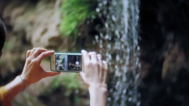 Mujer aventura de viaje tomando fotos de un teléfono inteligente en una cascada de montaña, disfrutando del hermoso paisaje de la naturaleza — Vídeo de stock