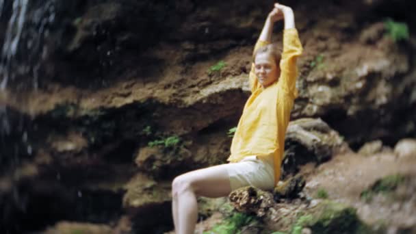 Junge Frau, die mit erhobenen Händen vor Wasserfall steht. Touristin mit ausgestreckten Armen beim Blick auf Wasserfall. — Stockvideo