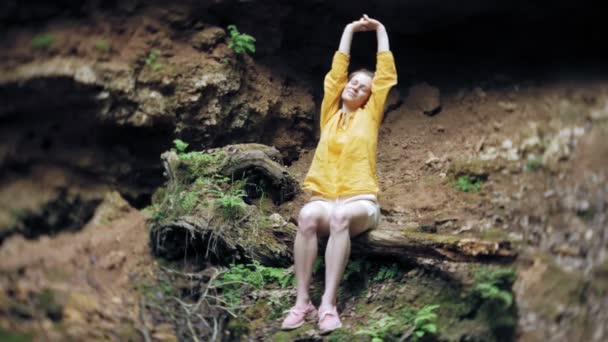 Mujer joven de pie frente a la cascada con las manos levantadas. Turista femenina con los brazos extendidos mirando la cascada . — Vídeo de stock