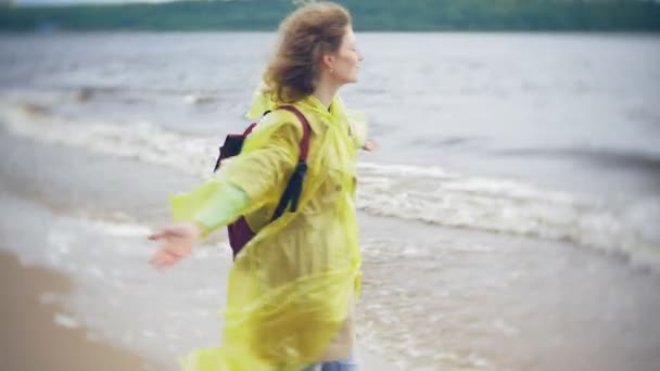 Счастливая женщина прогуливаясь вдоль побережья Путешествуя приключенческий отдых стиль жизни на открытом воздухе. Девушка в модном желтом плаще — стоковое видео