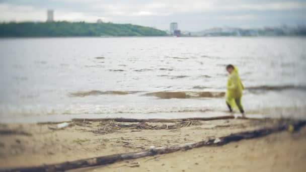 Menina feliz andando ao longo da costa Viajando Lifestyle aventura férias ao ar livre. Uma menina vestida com uma capa de chuva amarela elegante — Vídeo de Stock