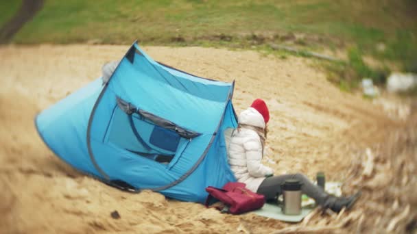 Tourist tent on the river bank. two girl sits near the tent eating and drinking looks at the river. — Stock Video