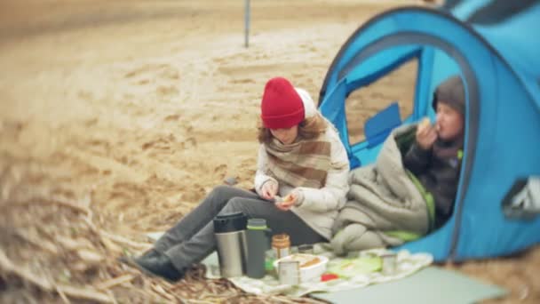 Turistický stan na břehu řeky. dvě dívka sedí u stanu, jídla a pití se dívá na řece. — Stock video