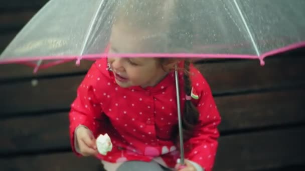 Pequena menina bonita com guarda-chuva jogando na chuva comendo sorvete na costa — Vídeo de Stock