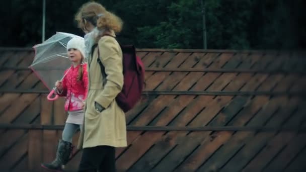 Kleines schönes Mädchen und ihre Mutter mit Regenschirm spielen im Regen — Stockvideo