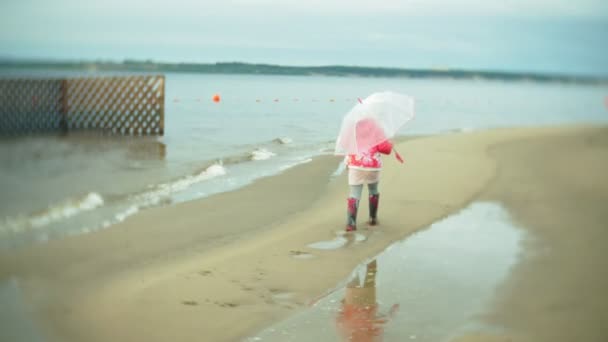 Petite belle fille avec parapluie, jouant sous la pluie, marchant le long de la côte — Video