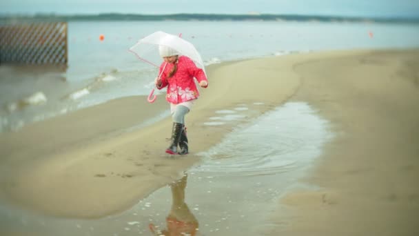 Mooi meisje met paraplu, spelen in de regen, wandelen langs de kust — Stockvideo
