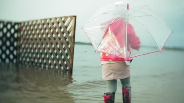 Όμορφο κοριτσάκι με ομπρέλα, παίζοντας στη βροχή, περπατώντας κατά μήκος της ακτής — Αρχείο Βίντεο