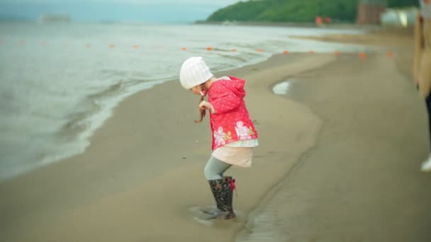 Маленькая красивая девочка с зонтиком, играющая под дождем, идущая вдоль побережья — стоковое видео