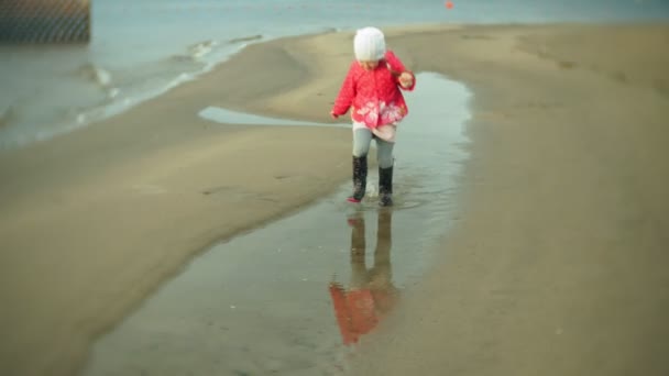 Kleines schönes Mädchen mit Regenschirm, im Regen spielend, entlang der Küste spazierend — Stockvideo