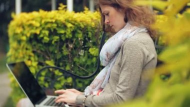 Kadın dizüstü bilgisayar ile güzel bir yeşil parkta bir bankta rahatlatır. Bir genç çok yıllık kadında bir dizüstü bilgisayar çalışan bir botanik bahçesi. Açık havada teknoloji