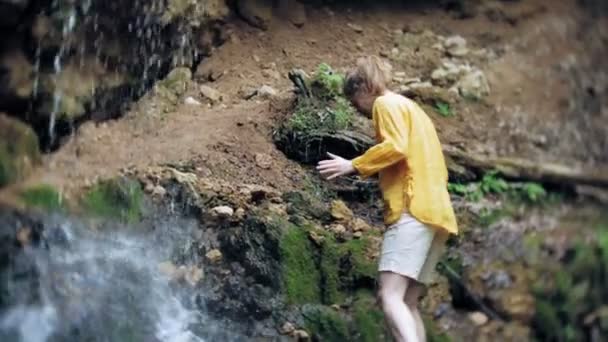 年轻女子站在瀑布前面 双手举起 女性游客张开双臂看着瀑布 — 图库视频影像