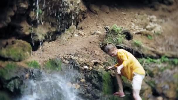 Young woman standing in front of waterfall with her hands raised. Female tourist with her arms outstretched looking at waterfall. — Stock Video