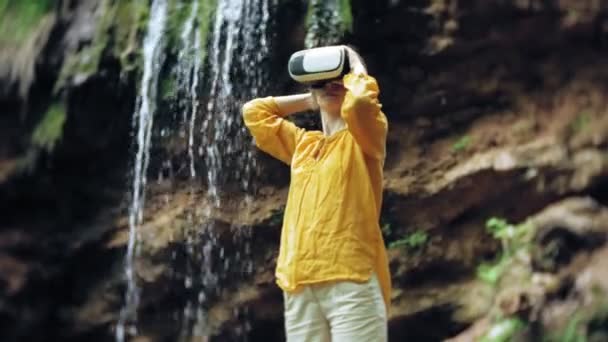 Fille réalité virtuelle lunettes VR ensoleillé jour faune femme levant les mains pics montagnes, cascade, forêt électronique portable technologie utilisant simulateur de jeu expérience visuelle 3d innovation cosmique — Video