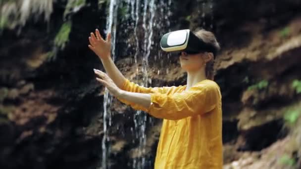 Fille réalité virtuelle lunettes VR ensoleillé jour faune femme levant les mains pics montagnes, cascade, forêt électronique portable technologie utilisant simulateur de jeu expérience visuelle 3d innovation cosmique — Video