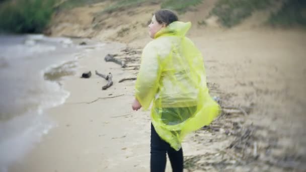 幸せな女の子のライフ スタイルの旅冒険休暇屋外の海岸に沿って歩きます。おしゃれな黄色のレインコートを着た女の子 — ストック動画