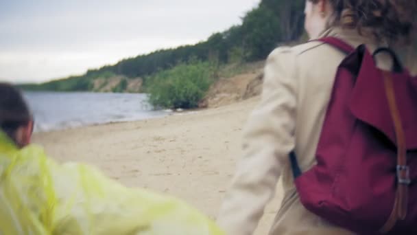 Chica feliz caminando a lo largo de la costa Viajar vacaciones aventura estilo de vida al aire libre. Una chica vestida con un impermeable amarillo de moda — Vídeos de Stock