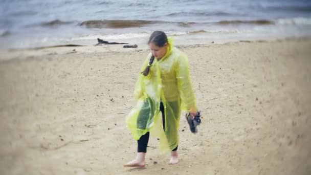 幸せな女の子のライフ スタイルの旅冒険休暇屋外の海岸に沿って歩きます。おしゃれな黄色のレインコートを着た女の子 — ストック動画