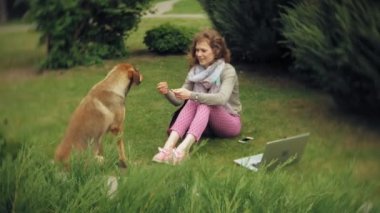 Bir kadın bir dizüstü bilgisayar ile güzel bir yeşil parkta çim çimenlikte köpeğiyle rahatlatır. Bir genç çok yıllık kadında bir dizüstü bilgisayar çalışan bir botanik bahçesi. Açık havada teknoloji