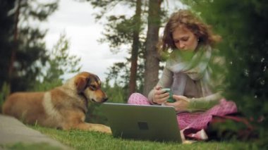 Bir kadın bir dizüstü bilgisayar ile güzel bir yeşil parkta çim çimenlikte köpeğiyle rahatlatır. Bir genç çok yıllık kadında bir dizüstü bilgisayar çalışan bir botanik bahçesi. Açık havada teknoloji
