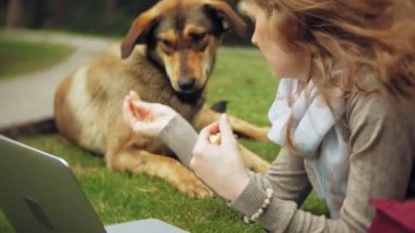 Bir kadın bir dizüstü bilgisayar ile güzel bir yeşil parkta çim çimenlikte köpeğiyle rahatlatır. Bir genç çok yıllık kadında bir dizüstü bilgisayar çalışan bir botanik bahçesi. Açık havada teknoloji