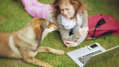 Bir kadın bir dizüstü bilgisayar ile güzel bir yeşil parkta çim çimenlikte köpeğiyle rahatlatır. Bir genç çok yıllık kadında bir dizüstü bilgisayar çalışan bir botanik bahçesi. Açık havada teknoloji