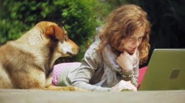 Bir kadın bir dizüstü bilgisayar ile güzel bir yeşil parkta çim çimenlikte köpeğiyle rahatlatır. Bir genç çok yıllık kadında bir dizüstü bilgisayar çalışan bir botanik bahçesi. Açık havada teknoloji