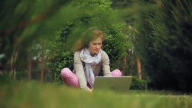 Kadın dizüstü bilgisayar ile çim çimen güzel yeşil park rahatlatır. Bir genç çok yıllık kadında bir dizüstü bilgisayar çalışan bir botanik bahçesi. Açık havada teknoloji