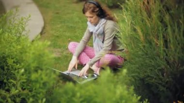 Kadın dizüstü bilgisayar ile çim çimen güzel yeşil park rahatlatır. Bir genç çok yıllık kadında bir dizüstü bilgisayar çalışan bir botanik bahçesi. Açık havada teknoloji