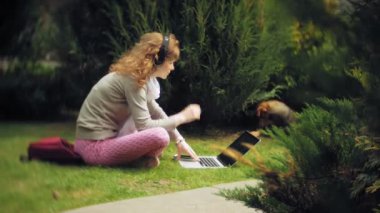 Bir kadın bir dizüstü bilgisayar ile güzel bir yeşil parkta çim çimenlikte köpeğiyle rahatlatır. Bir genç çok yıllık kadında bir dizüstü bilgisayar çalışan bir botanik bahçesi. Açık havada teknoloji