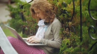 Kadın dizüstü bilgisayar ile güzel bir yeşil parkta bir bankta rahatlatır. Bir genç çok yıllık kadında bir dizüstü bilgisayar çalışan bir botanik bahçesi. Açık havada teknoloji