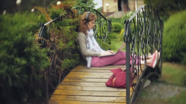 ラップトップを持つ女性は、美しい緑豊かな公園のベンチで寛ぎます。ノート パソコンの背後に働く植物園の多年生若い女性。オープンエアの技術 — ストック動画
