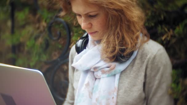 노트북과 여자 아름 다운 녹색 공원에서 벤치에 이완 한다. 노트북 뒤에 작동 하는 수목원에서 다년생 젊은 여자. 야외에서 기술 — 비디오